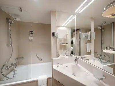 Ein modernes Badezimmer an Bord der MSC World America. Es zeigt ein Waschbecken mit Spiegel, eine Dusch-Badewannen-Kombination und helle Oberflächen.