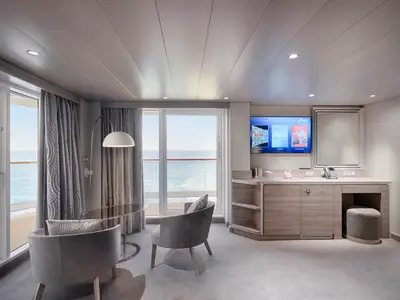 Geräumige Grand Suite Aurea mit Terrasse und Meerblick an Bord der MSC World America. Moderner Wohnbereich mit Sesseln, Tisch und TV.