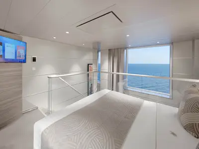 Blick in eine helle, moderne zweigeschossige Suite der MSC World America. Im Vordergrund ein Doppelbett, dahinter ein TV und ein großes Fenster mit weitem Meerblick.