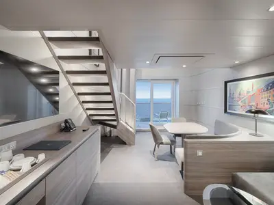 Eine moderne, helle zweistöckige Suite an Bord der MSC World America mit Treppe, Wohnbereich, Esstisch und Balkon mit Meerblick.