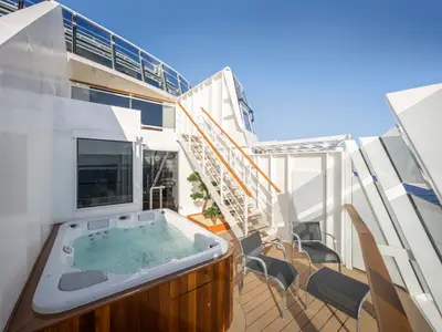 Private Außenterrasse einer Duplex Suite an Bord der MSC World America. Auf dem Holzdeck stehen ein sprudelnder Whirlpool, Sonnenliegen und eine Treppe. Blauer Himmel ist sichtbar.