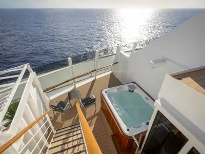 Die private Terrasse einer Suite an Bord der MSC World America mit einem sprudelnden Whirlpool, zwei Liegestühlen und direktem Meerblick bei strahlendem Sonnenschein.