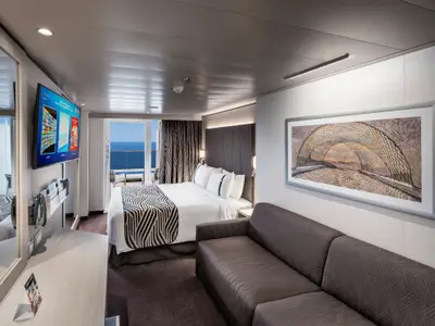 Eine moderne Balkonkabine an Bord der MSC World Asia mit Doppelbett, Sofa und direktem Meerblick von einem privaten Balkon. Die Einrichtung ist hell und einladend.
