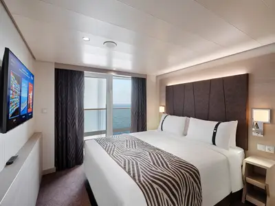 Helle Balkonkabine an Bord der MSC World Asia mit grossem Doppelbett und stilvollem Interieur. Eine Fenstertür führt auf einen Balkon mit weitem Meerblick.