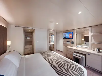 Helle Balkonkabine an Bord der MSC World Asia. Doppelbett, Schreibtisch mit TV, Spiegel und offener Kleiderschrank. Modernes Design, Holzdetails, indirekte Beleuchtung.