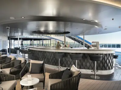 Die Zen Bar an Bord der MSC World Asia mit geschwungener Theke, dunklen Barhockern und bequemen Lounge-Sesseln. Blick auf das offene Meer.