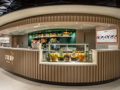 Eine moderne, halbrunde Theke der Zest Juice Bar an Bord der MSC World Asia. Auf der Theke und in Regalen dahinter sind Körbe mit frischem Obst, Flaschen und Gläser zu sehen. Die Bar hat eine helle Holzverkleidung und eine grüne Wand im Hintergrund.