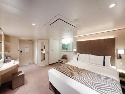 Helle, barrierefreie Innenkabine an Bord der MSC World Asia mit einem großen Doppelbett, Nachttischen, einem Schminktisch und einer Tür zum Badezimmer. Der Raum ist in warmen Brauntönen und hellem Holz gehalten.