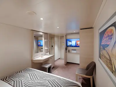 Eine helle Innenkabine an Bord der MSC World Asia. Sie zeigt ein Bett mit Zebra-Muster, einen Schminktisch mit Spiegel und einen Fernseher an der Wand.