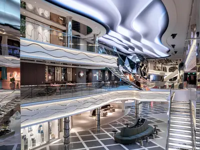 Blick auf die mehrstufige World Galleria an Bord der MSC World Asia. Die moderne Architektur zeigt geschwungene Balustraden, eine beleuchtete Decke, glänzende Oberflächen, Restaurants und Boutiquen auf mehreren Ebenen.