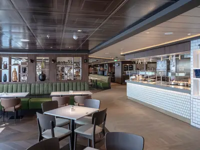 Das moderne Buffetrestaurant an Bord der MSC World Asia zeigt grüne Sitzbänke, Esstische und eine lange, weiss geflieste Theke mit Speisen und Tellern.