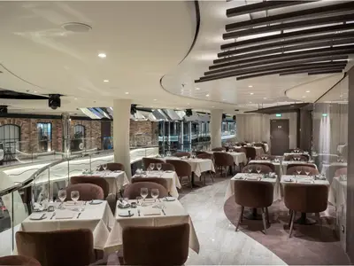 Modernes Restaurant an Bord der MSC World Asia mit gedeckten Tischen und braunen Stühlen. Blick auf eine Promenade im Backstein-Stil.