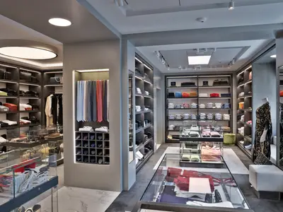 Elegante Boutique an Bord der MSC World Asia. Beleuchtete Regale mit Kleidung, Krawatten und Handtaschen. Glasvitrinen zeigen Accessoires. Moderne Einrichtung.