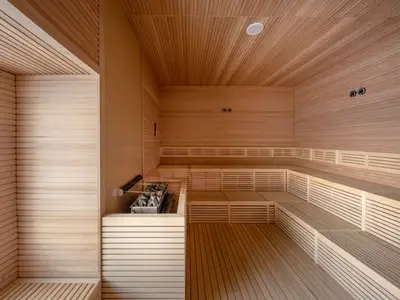 Eine helle, moderne Sauna an Bord der MSC World Asia. Der Raum ist komplett mit hellem Holz verkleidet und verfügt über mehrstufige Sitzbänke und einen Saunaofen mit Steinen.