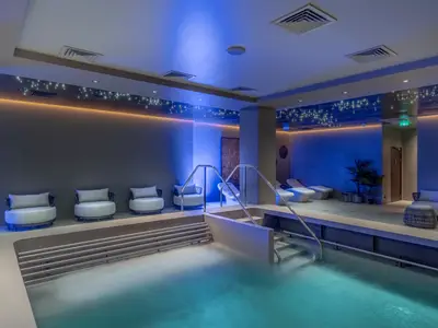 Ein moderner Thermalbereich an Bord der MSC World Asia mit einem Innenpool, bequemen Liegen und Sesseln. Blaue und warme Lichttöne erzeugen eine entspannte Atmosphäre, ergänzt durch einen sternenähnlichen Lichteffekt an der Decke.