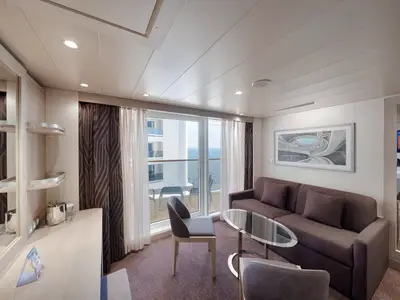 Moderne Suite an Bord der MSC World Asia mit beigem Interieur, großem Sofa, Glastisch und Zugang zum Balkon mit Meerblick.