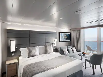 Eine helle und moderne MSC Yacht Club Deluxe Suite an Bord der MSC World Asia mit grosszügigem Doppelbett, Sofa, Sitzbereich und einem Balkon mit Blick auf das offene Meer.