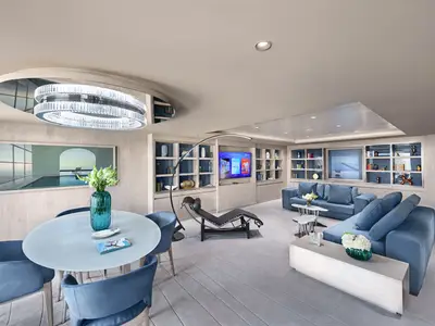 Innenansicht der luxuriösen Owner's Suite an Bord der MSC World Asia mit modernem Essbereich, blauen Sesseln und Sofas, elegantem Kronleuchter und vielen Regalen mit Dekoration.