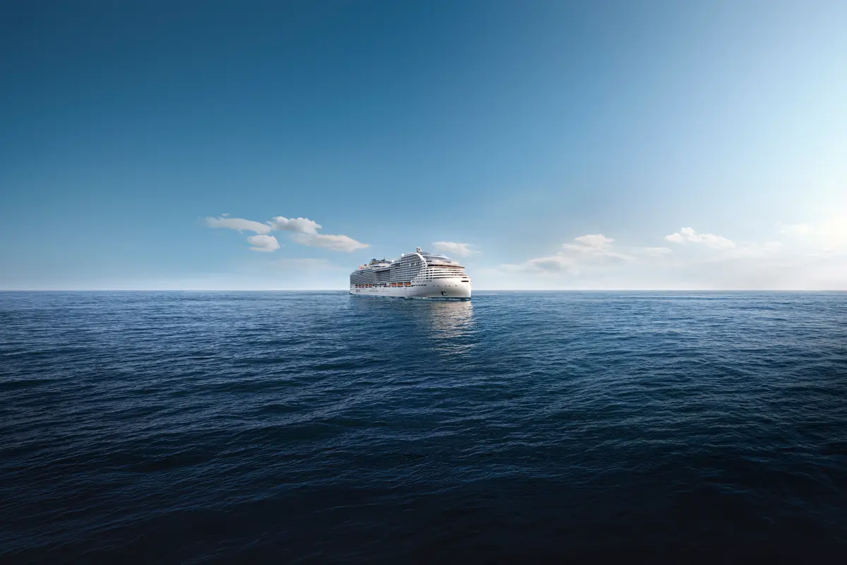 Die MSC World Atlantic, ein modernes Kreuzfahrtschiff, fährt auf dem weiten, blauen Meer. Blauer Himmel mit einigen Wolken. Sonnenlicht kommt von rechts.