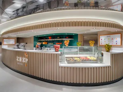 Eine helle, moderne Saftbar namens Zest an Bord der MSC World Atlantic. Die Theke ist aus hellem Holz mit vertikalen Lamellen gefertigt und präsentiert frisches Obst sowie Saftpressen. Eine grüne Wand dient als Hintergrund mit Regalen voller Obstkörbe.