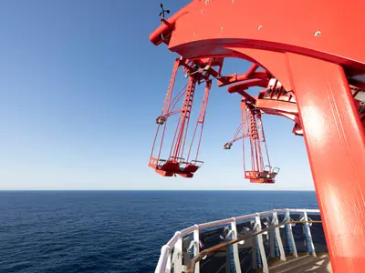 Der rote 'Cliffhanger', ein Schaukelfahrgeschäft, ragt auf der MSC World Atlantic über das weite blaue Meer. Einzelne rote Sitze hängen an massiven roten Stahlstreben vor dem Horizont.
