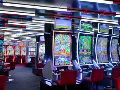 Blick in das stilvolle Casino der MSC World Atlantic mit zahlreichen Slot-Maschinen in leuchtenden Farben und roten Barhockern. Das moderne Interieur ist von der Decke bis zum Boden beleuchtet und spiegelt sich wider.