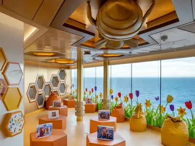 Ein farbenfroher Kinderbereich an Bord der MSC World Atlantic. Bienen-Thema, mit Waben an Wänden und Decke, Sitzsäcken und Puzzles. Grosse Fenster mit Blumen-Dekor und Meerblick.