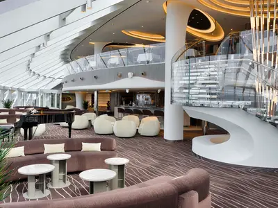 Blick in die moderne, zweistöckige Top Sail Lounge mit Bar, bequemen Sitzecken, Flügel und Wendeltreppe an Bord der MSC World Atlantic.