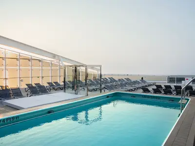 Der ruhige Zen Pool an Deck der MSC World Atlantic, umgeben von Liegestühlen unter einer Überdachung. Diffuses Sonnenlicht spiegelt sich im Meer im Hintergrund. Pooltiefe: 1.80m / 5ft 9in.