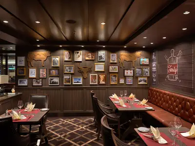 Das Spezialitätenrestaurant Butcher's Cut an Bord der MSC World Atlantic. Dunkle Holzwände, Ledersofas und gedeckte Tische mit roten Läufern. Gerahmte Bilder und Rindergrafiken schmücken die Wände.
