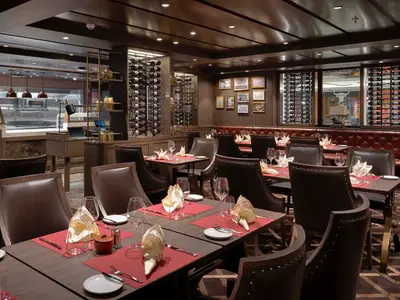 Ein luxuriöses Spezialitätenrestaurant, Butcher's Cut, an Bord der MSC World Atlantic mit elegant gedeckten Tischen und Weinflaschen in wandhohen Regalen. Keine Personen sichtbar.