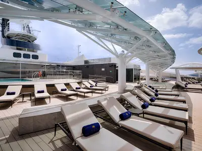 Sonnendeck und Pool des MSC Yacht Club an Bord der MSC World Atlantic. Reihen von Liegestühlen unter einer modernen Glasdachkonstruktion. Im Hintergrund sind Teile des Schiffes und der Himmel sichtbar.