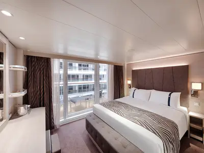 Eine modern eingerichtete Balkonkabine an Bord der MSC World Europa mit großem Doppelbett. Der Blick fällt auf einen privaten Balkon mit Outdoor-Möbeln und der Schiffsumgebung.