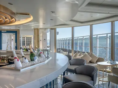 Elegante Champagne-Bar 'Fizz' an Bord der MSC World Europa mit Bartheke, gekühlten Flaschen und Loungesesseln. Große Fenster bieten einen weiten Blick auf das offene Meer.
