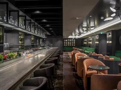 Innenansicht der Elixir Mixology Bar auf der MSC World Europa. Links eine lange Bar mit Flaschen und Pflanzen, rechts ein Lounge-Bereich mit braunen und grünen Sitzen.