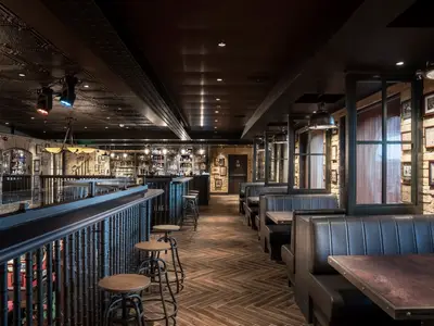 MSC World Europa, Bar The Gin Project: Tresen, Barhocker, Sitzbaenke, Tische. Ziegelsteinwaende mit Bildern, dunkle Decke mit Beleuchtung.