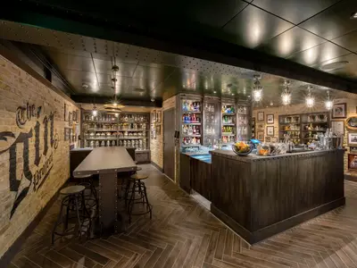 Die rustikale Bar 'The Gin Project' an Bord der MSC World Europa. Backsteinwände, dunkle Holzmöbel und Regale voller Gin-Flaschen. Bartresen und Stehtische sind gut beleuchtet.