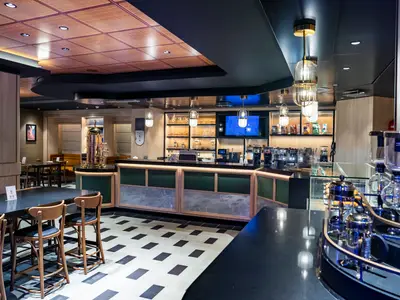 Innenansicht des Coffee Emporium an Bord der MSC World Europa mit stilvoller Theke, Sitzgelegenheiten, Kaffeemaschinen und dekorativer Beleuchtung.