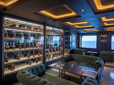 Die elegante Bar/Lounge an Bord der MSC World Europa bietet beleuchtete Glasvitrinen mit Spirituosen und dunkelgrüne Sofas mit Meerblick.