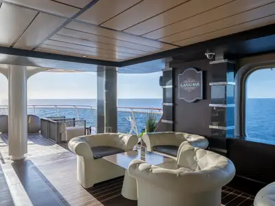 Die helle Lanai Bar an Bord der MSC World Europa mit bequemen Polstersesseln und Tischen. Im Hintergrund öffnet sich der Bereich zum Meer und einem Außendeck.