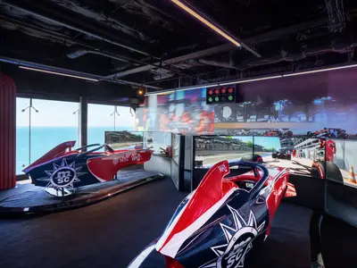 Zwei moderne F1-Simulatoren in einem Unterhaltungsbereich an Bord der MSC World Europa. Große Bildschirme zeigen Rennszenen, während durch Fenster das Meer zu sehen ist.