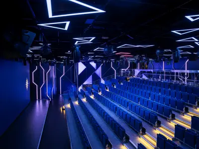 Ansicht der futuristischen MSC Luna Park Arena an Bord der MSC World Europa. Blaue Sitzreihen und neonbeleuchtete Wände mit geometrischen Mustern. Eine dynamische Stimmung für Shows.