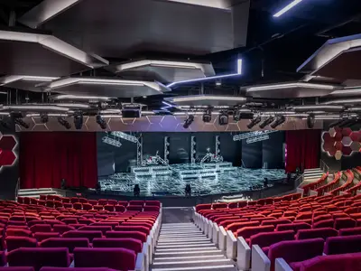 Das World Theatre der MSC World Europa zeigt eine futuristische Bühne mit drei Motorrädern auf beleuchteten Podesten und roten Samtsitzen im Vordergrund, bereit für eine Show.