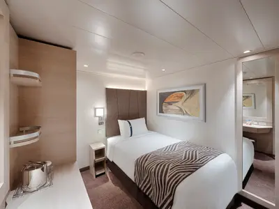 Einzelkabine an Bord der MSC World Europa. Mit Einzelbett, Nachttisch, Kunstwerk und Spiegel. Helle, moderne Einrichtung in Holzoptik.