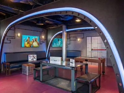 Ein lebhaftes Unterhaltungszentrum an Bord der MSC World Europa. Der Raum im Steampunk-Stil bietet Sofas, große Bildschirme, ein VR-Headset und einen Airhockey-Tisch.