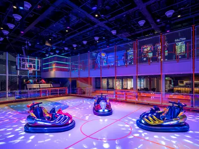 Der Sportplex an Bord der MSC World Europa zeigt eine Arena mit drei farbigen Bumper Cars und einem Basketballkorb. Die Szene ist von farbigen Lichtern und Neonakzenten beleuchtet.
