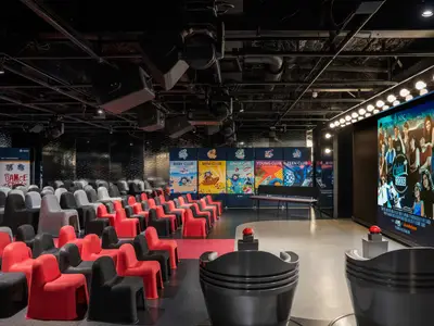 Moderner Kinder- und Jugendclub-Bereich an Bord der MSC World Europa. Rote und schwarze Sitze, Bühne mit Spielpulten, Club-Banner und großer Bildschirm.