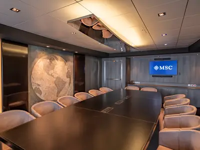 Moderner Konferenzraum an Bord der MSC World Europa. Langer, dunkler Tisch, viele Stühle, Bildschirm mit MSC Logo. Eine große Weltkarte ist an der Wand zu sehen.