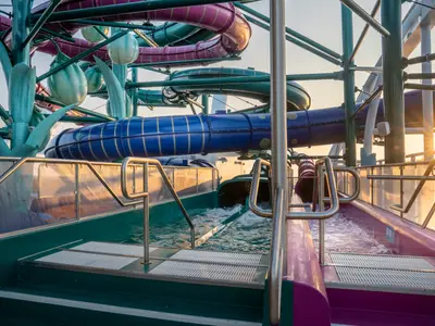 Wasserrutschen des Aurora Borealis Aquaparks der MSC World Europa. Blaue und violette Rutschen münden in einen Poolbereich. Die warme Abendsonne beleuchtet das Deck und das Wasser.