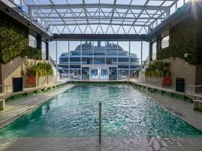 Der lichtdurchflutete Botanic Garden Pool an Bord der MSC World Europa. Innenpool mit Glasdach, grünen Wänden, Pflanzen. Blick auf das Außendeck.